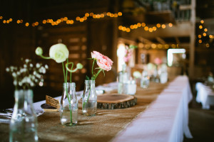 Sharing stories at a Wedding Table, Rustic pink and white flower in jars, burlap runners, candles , globe lights in barn. 