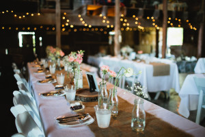 Sharing stories at a Wedding Table, Rustic pink and white flower in jars, burlap runners, candles , globe lights in barn. 